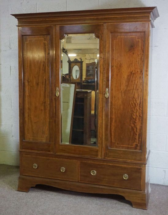 An Edwardian mahogany and satinwood banded triple wardrobe, with mirrored central door, over two