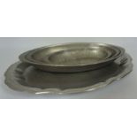 Four graduated pewter serving dishes, together with a larger scalloped tray and a brass helmet