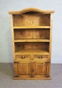 A modern waxed pine open side cabinet, with an arched top, two shelves and drawers and cupboards