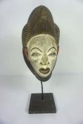 An African tribal carved and painted mask, with ornate hairpiece and white painted face and red