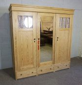 A stripped pine triple wardrobe, early 20th century, with mirrored central door, with three small