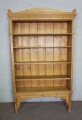 A stripped pine open bookshelf with adjustable shelving, raised on short legs with bracket supports,