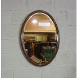 An Edwardian oval mirror on stand, with curved supports, 73cm high, 82cm wide; and another oval