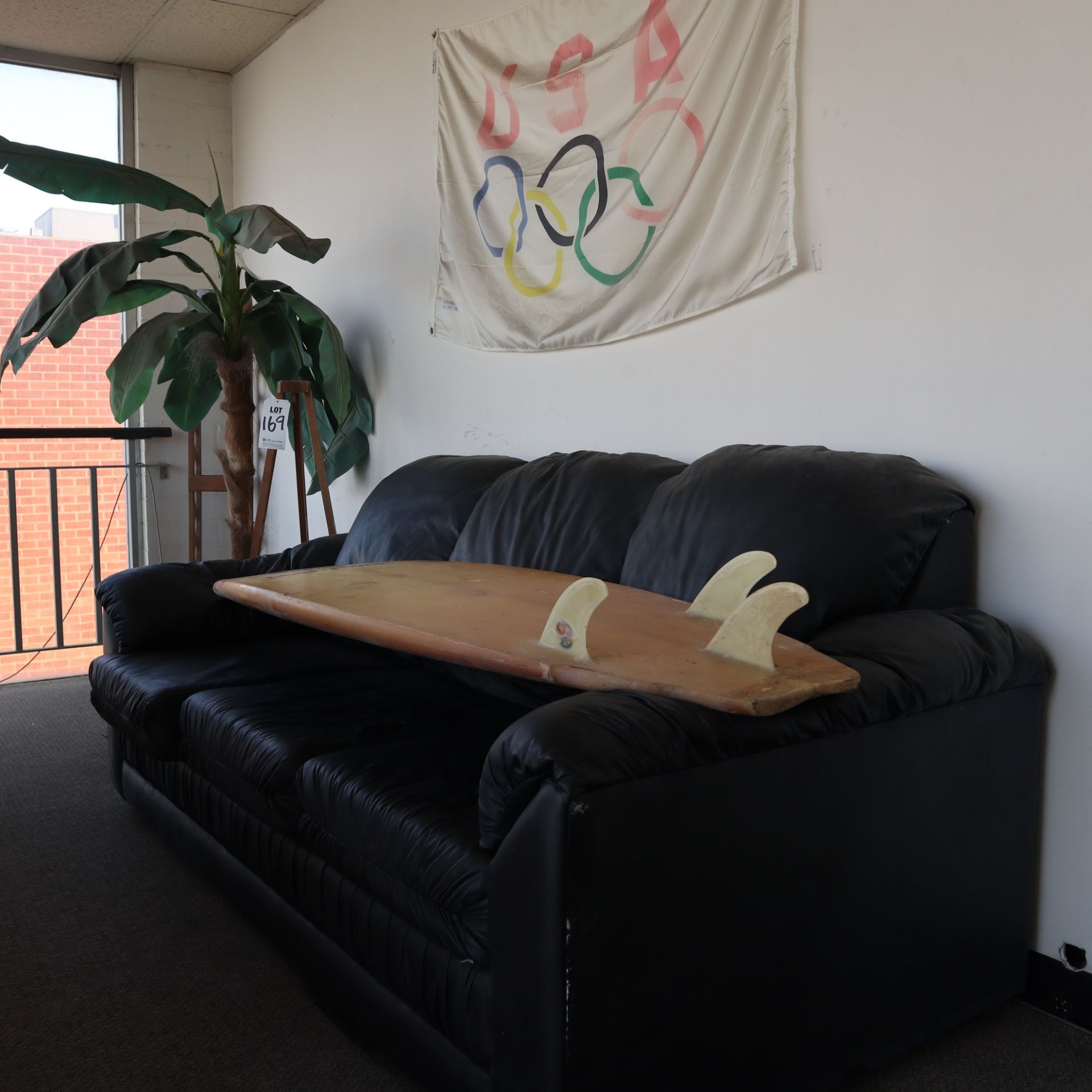 UPSTAIRS LOUNGE AREA TO INCLUDE: (1) BLACK SOFA, (1) SURFBOARD, (1) DECORATIVE PALM TREE