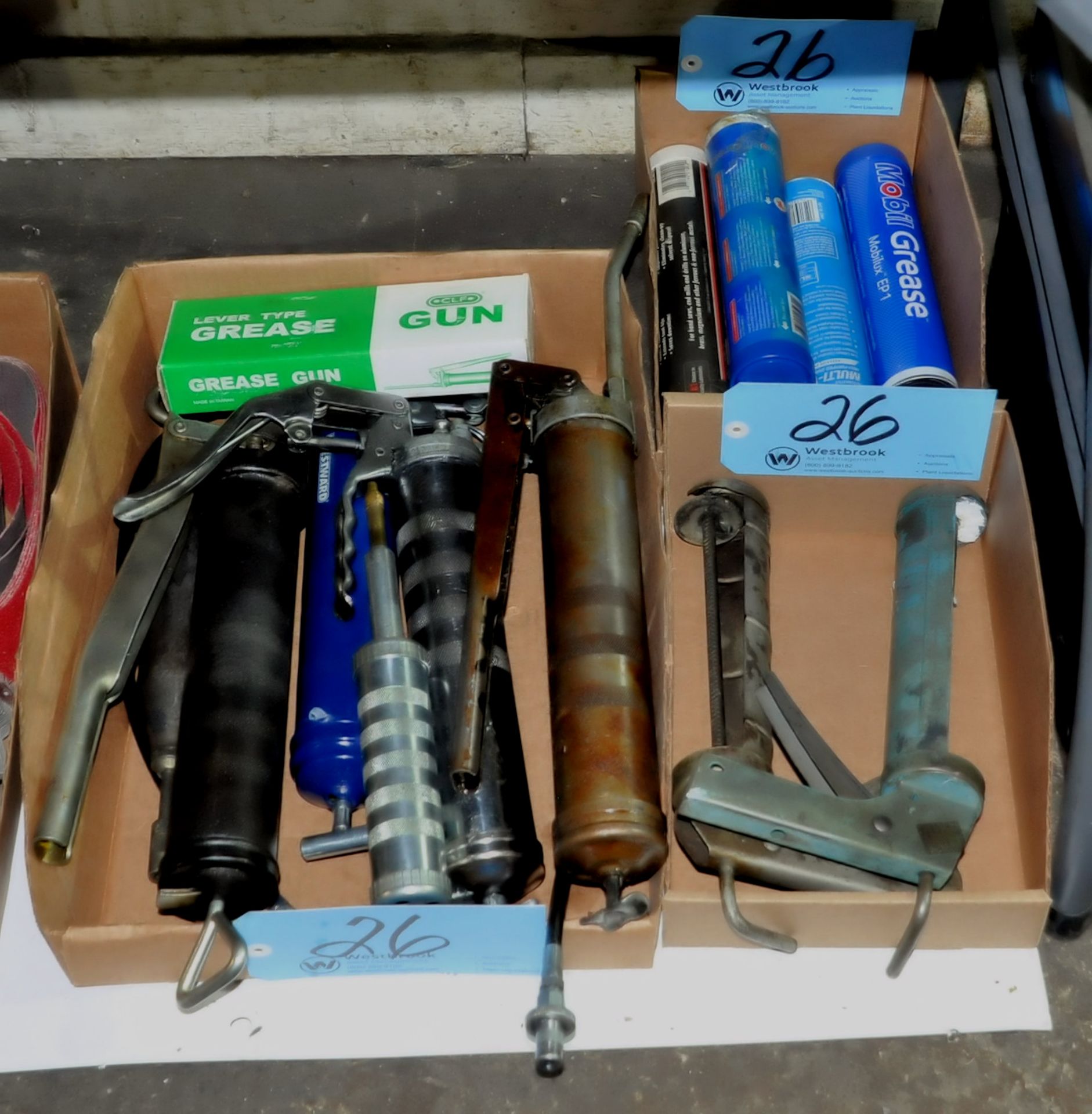 Lot-Grease Guns and Grease with Caulk Guns in (3) Boxes on Floor Under (1) Table