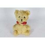 A mohair teddy bear with glass eyes. Bear has a red bow-tie. Bear is 14 cm in height.