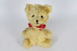 A mohair teddy bear with glass eyes. Bear has a red bow-tie. Bear is 14 cm in height.