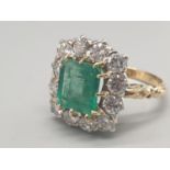An 18 K yellow and white gold ring with an emerald cut emerald central stone surrounded by a dozen