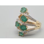 An 18 K yellow gold ring with six oval faceted emeralds, arranged between three rows of diamonds.