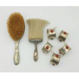 An antique pair of silver brushes (London hallmarked) AND Five white metal napkin rings with red