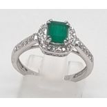 An 18K White Gold Diamond and Emerald Ring. Centre emerald surrounded by diamonds. H-VS Grade.