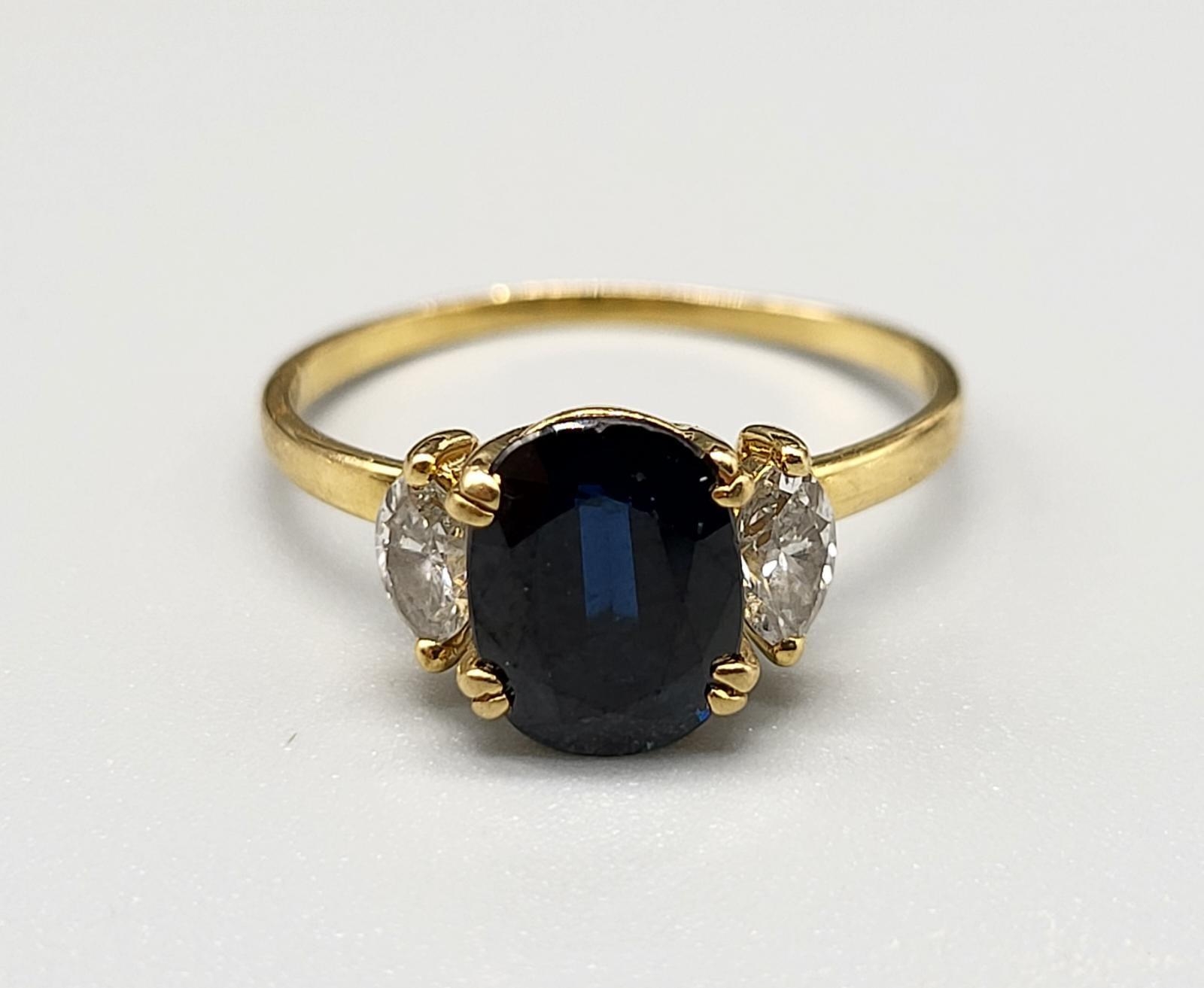 An 18 K yellow gold ring with an oval cut dark blue sapphire, flanked by two marquise cut sapphires.