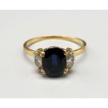 An 18 K yellow gold ring with an oval cut dark blue sapphire, flanked by two marquise cut sapphires.