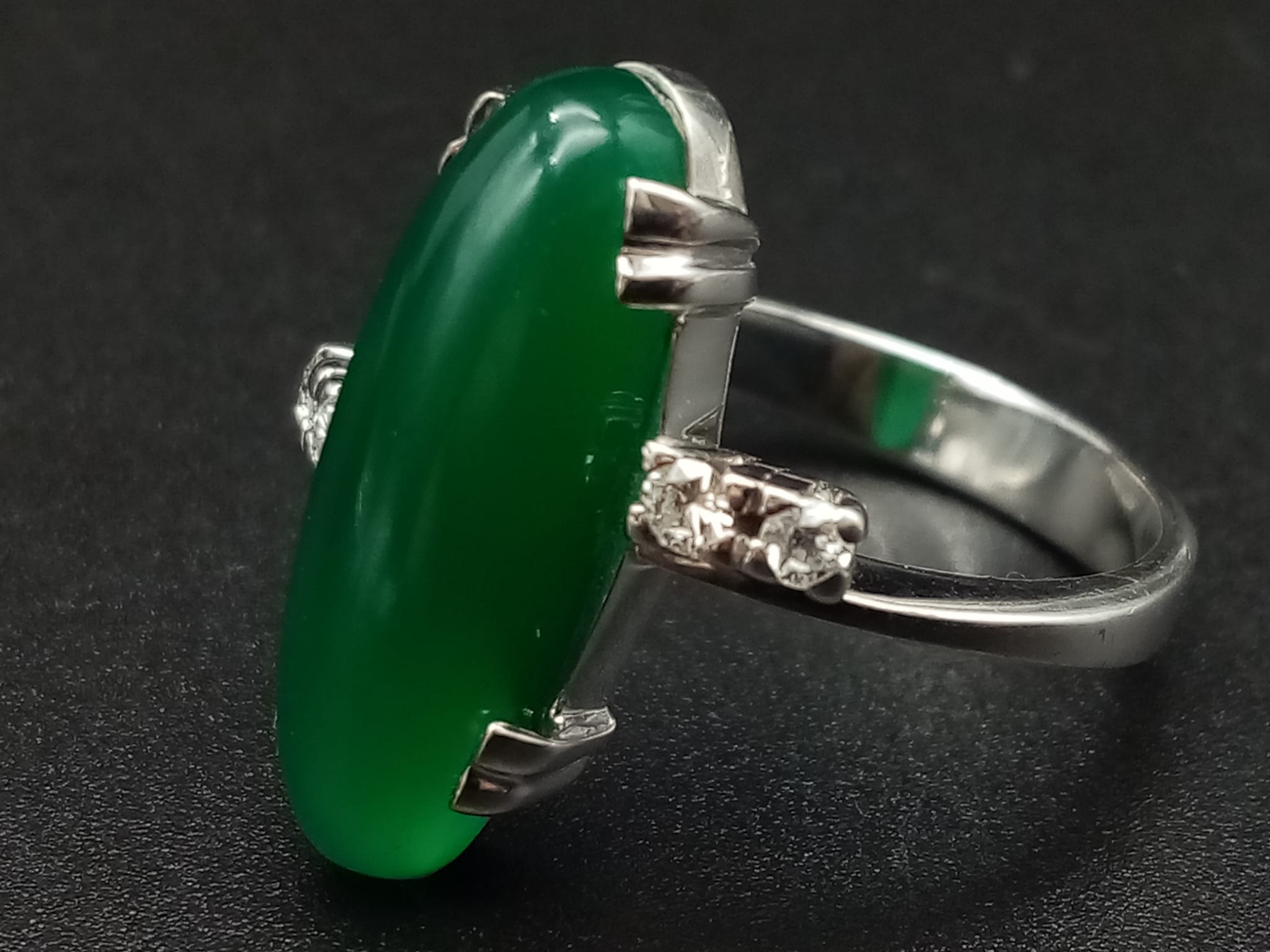 An 18K White Gold (tested) Jade and Diamond Ring. Large oval jade centre stone with two small