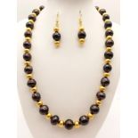 A natural black pearl necklace and earrings set with 18 K yellow gold plated beads. Pearl size: 10-