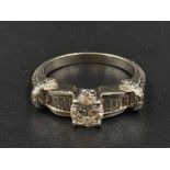 A Platinum Diamond Ring - Central stone with small baguette-cut diamonds on shoulders. Size M. 7.86g