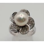 An attractive 18 K white gold ring with a diamond studded flower on top and a genuine round white