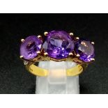 An 18K Yellow Gold and Large Three-Stone Amethyst and Diamond Ring. Three central intense clean