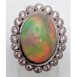An 18K white gold ring with a large cabochon natural opal (est 6-7 carats) surrounded by a halo of