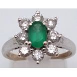 An 18K White Gold Emerald and Diamond Ring. Central oval emerald - 0.5ct surrounded by eight