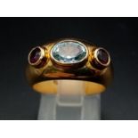AN 18K YELLOW GOLD RING WITH AQUAMARINE CENTRE STONE FLANKED EITHER SIDE BY 2 GARNETS . 9.7gms