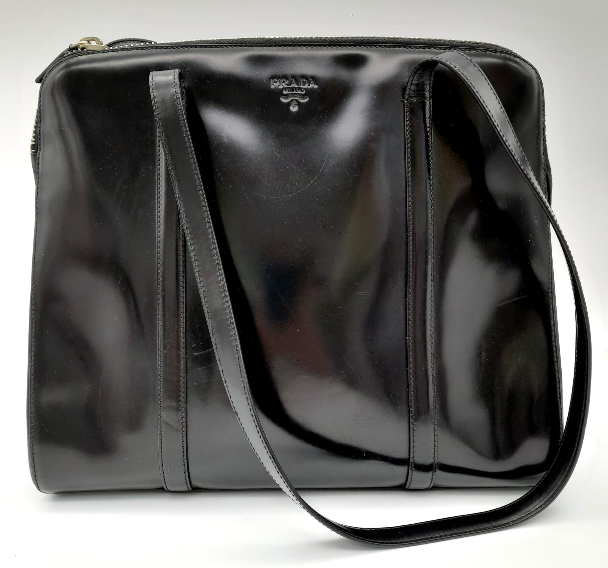 A Prada Patent Black Leather Shoulder Bag. Prada branding on exterior. Cloth monogram interior with