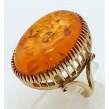 A 9K Yellow Gold Amber Ring. A large natural amber cabochon set in pierced decorative gold. Wonderfu