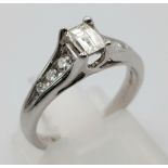 An 18K White Gold Emerald Cut Diamond Ring. 0.5ct central diamond with three graduated round cut dia