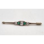 A 14K White Gold Emerald and Diamond Bar Brooch. Central round cut diamond flanked by an emerald and