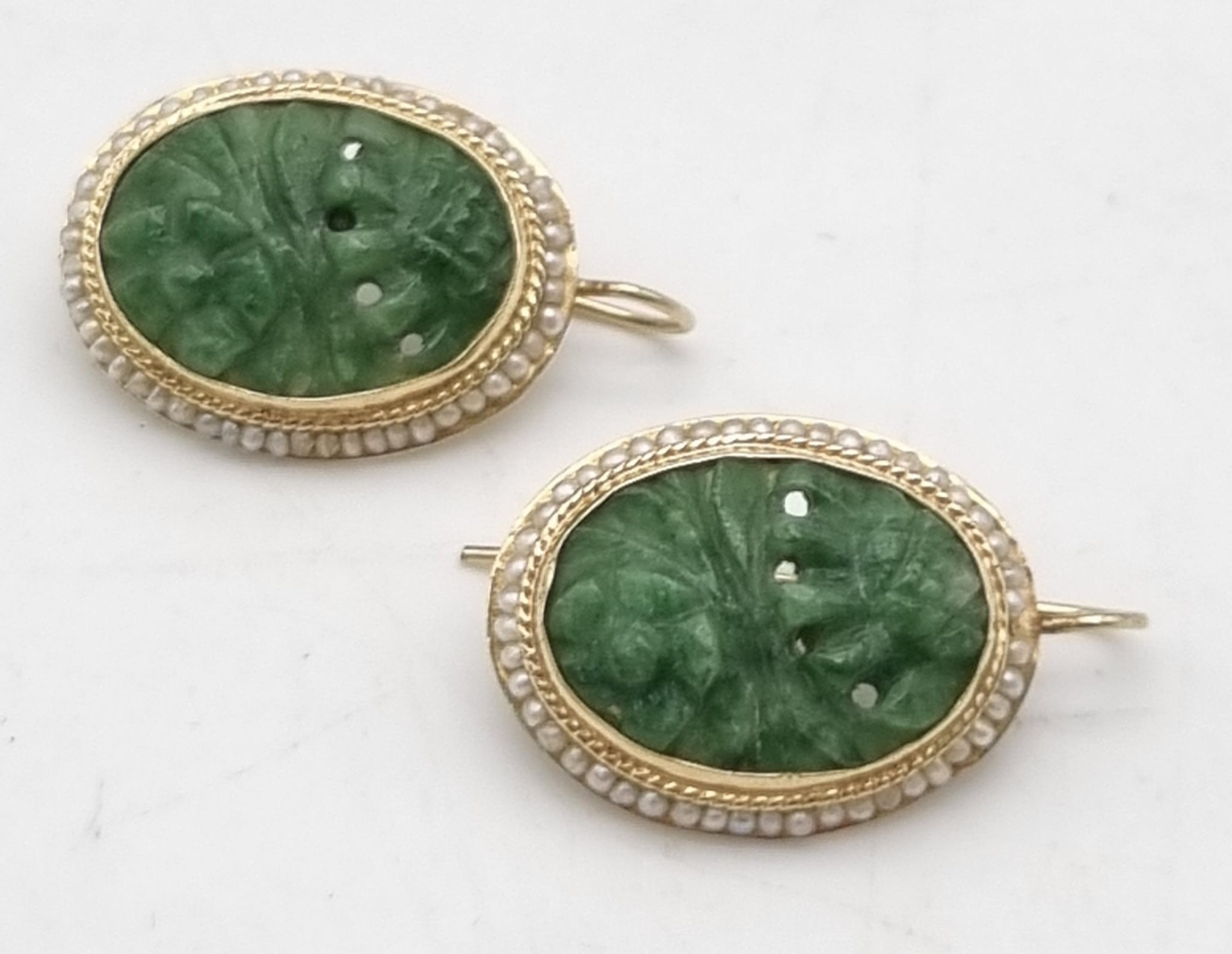 A vintage 14k yellow gold pair of earrings with carved oval jade surrounded by seed natural pearls.
