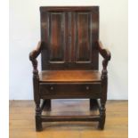 An oak Wainscot armchair, with a panel back and seat above a drawer, on turned legs united by