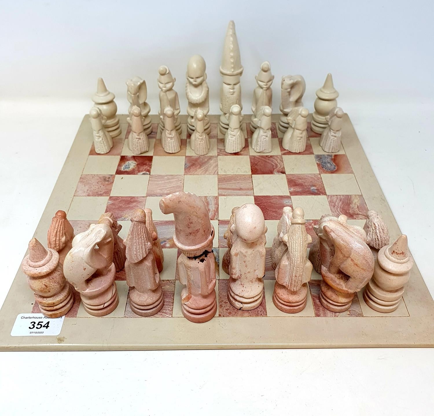 A carved stone pink and white chess set, with a board