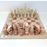 A carved stone pink and white chess set, with a board