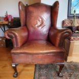 A George III style wing armchair, upholstered in leather, on cabriole front legs, with claw and ball