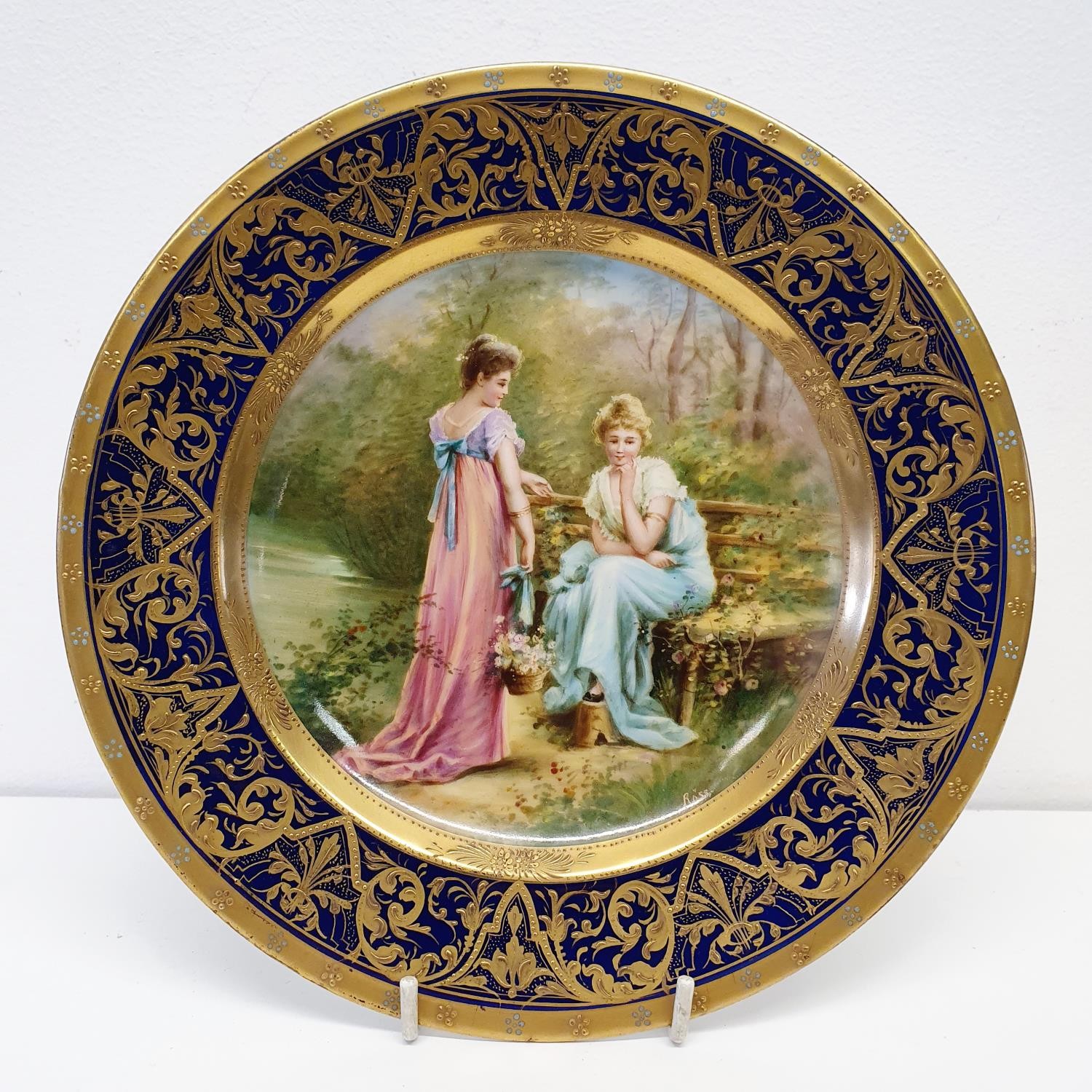 A Vienna porcelain plate, Liebesgeheimnis, within a blue and gilt border, 21 cm diameter Gilt a