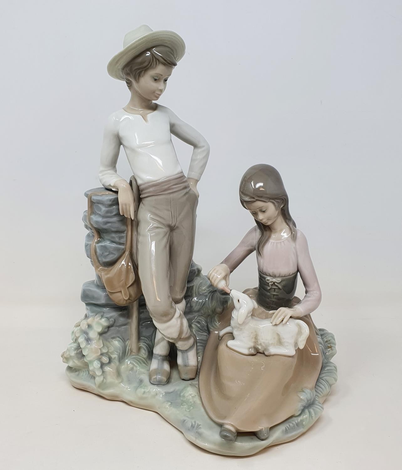 A Lladro group, of a young couple feeding a lamb, 28 cm high No chips cracks or restoration found