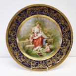 A Vienna porcelain plate, Amors Studium, within a blue and gilt border, 24.5 cm diameter No chips or