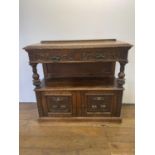 An oak buffet, the top having two drawers, above an open section, above two cupboard doors, carved