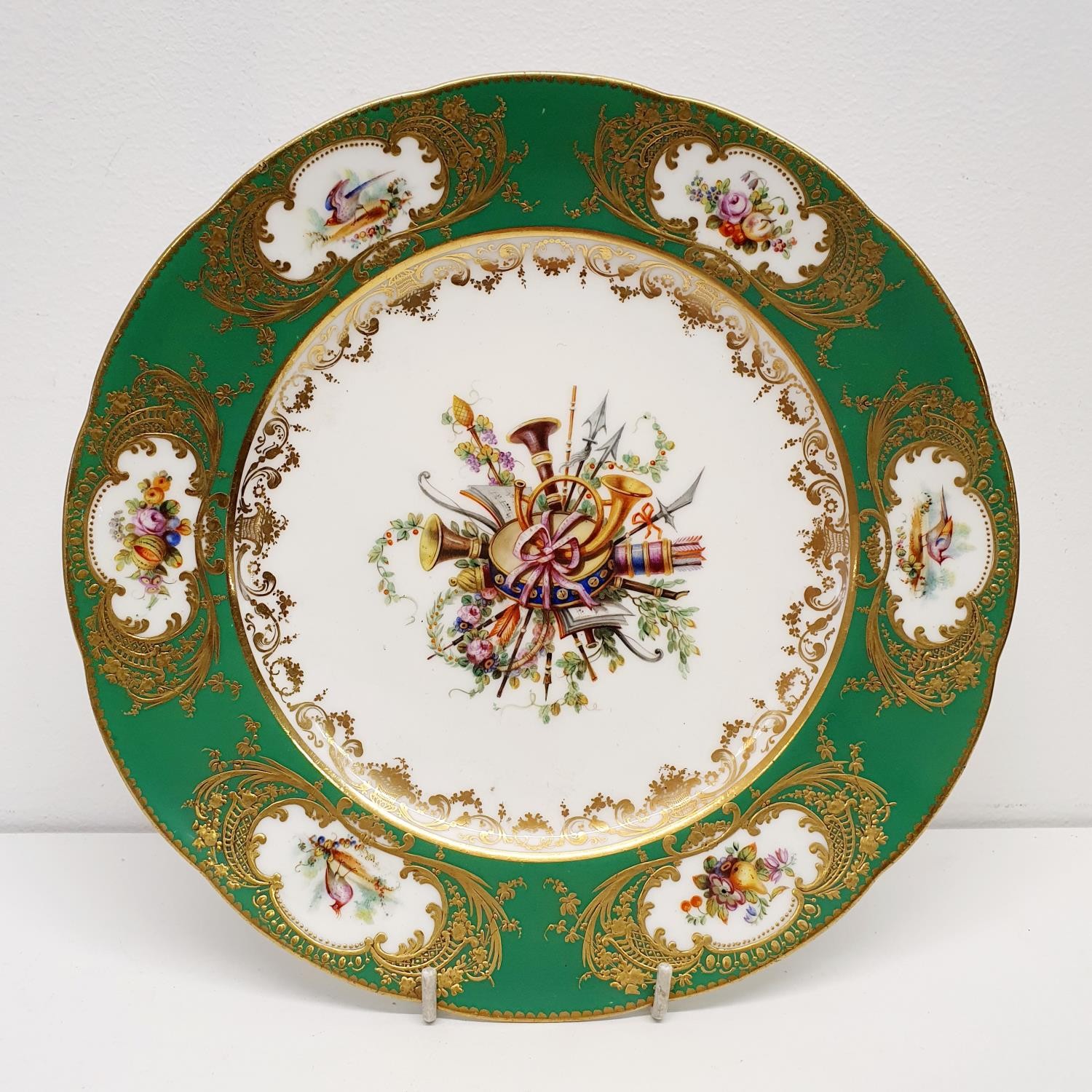 A Sevres style plate, decorated musical instruments and foliage, within a green and gilt border,