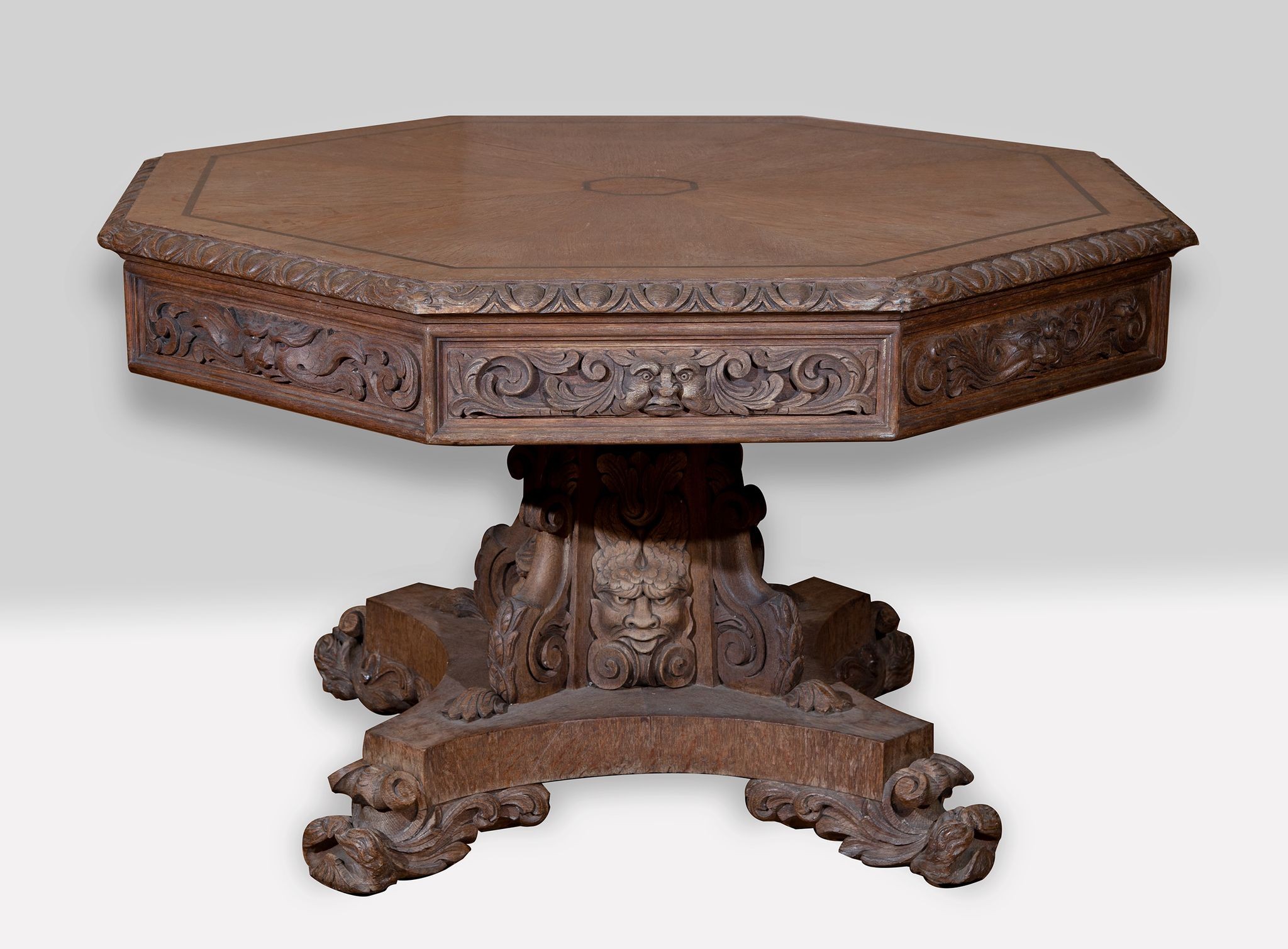 A late 19th/early 20th century carved oak drum top table, decorated masks and foliate forms, on a