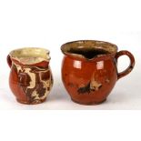 A slipware pottery jug, 14cms high; together with another similar smaller, 13cms high (2).