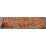 A Turkish hand knotted woollen runner with repeated floral motifs on a blue ground within a multi