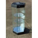A modern glass shop display cabinet of hexagonal form with three shelves and mirrored base, 40cms