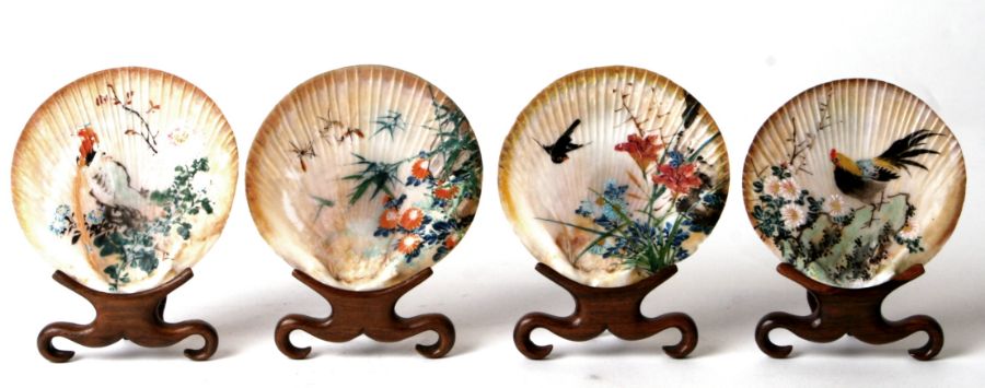 A set of four Chinese shells, each individually decorated with exotic birds and flowers, on hardwood
