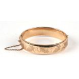 A 9ct gold hinged bangle with engraved foliate decoration to one half, 18.9g.