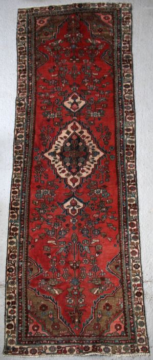A Persian Hamadan hand knotted woollen runner with central motif within a stylised border on a red