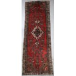 A Persian Hamadan hand knotted woollen runner with central motif within a stylised border on a red