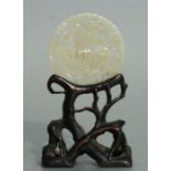 A Chinese pierced jade bi disc decorated with a stylised bird, mounted on a naturalistic hardwood