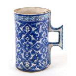 A Turkish / Iznik pottery tankard decorated with foliate scrolls on a blue ground, 21cms high.