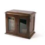 An early 20th century oak smoker's cabinet, the pair of glaze doors enclosing a fitted interior,